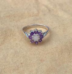 This beautiful opal and amethyst cluster ring has a 4.2mm round opal centre stone. With 8 round amethysts surrounding it measuring 2.25mm. Made from solid 925 sterling silver in Birmingham's historic Jewellery Quarter. The ring is available in a wide range of sizes. If your size isn't listed however please contact us and we will see if we can help you! There is a size conversion chart in our pictures!  If you are unsure of your ring size, you can order a ring sizer of us at https://etsy.me/33OVs Amethyst Cluster Gemstone Jewelry, Purple Opal Ring Gift, Purple Opal Gemstone Jewelry, Amethyst Gemstones With Halo Setting, Round Amethyst Gemstones With Halo Setting, Purple Opal Round Jewelry, Purple Opal Promise Ring, Amethyst Cluster Rings With Gemstone, Amethyst Cluster Gemstone Rings