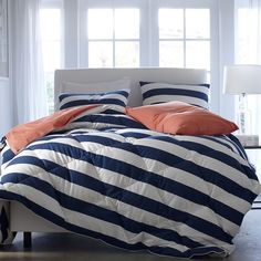 a bed with blue and white striped comforter next to a lamp on a table