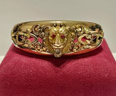 Antique gold filled bangle bracelet made circa 1895 with a lion's head and simulated jeweled eyes and mouth, signed by the maker on the inside. An incredible Victorian era fine lion motif bracelet! ERA - Circa 1880s / Victorian Era METAL / MATERIAL / Yellow gold filled, Simulated Rubies and diamonds  MARKINGS / HISTORY - F M Co. (The Finberg Manufacturing Company was headquartered in Attleboro, Mass. They were quite prolific and made gold filled jewelry like lockets and bangle bracelets in the styles of the era.)   CONDITION - Good antique condition. Gold filled metal has been cleaned and polished. Simulated gems are all intact. Amazing antique Victorian bracelet!  MEASUREMENTS - Inner circumference: 7 inches, Height of front of bracelet: 1 1/8 inches, Width of back of bracelet: 1/2 inch, Luxury Victorian Gold Bangle, Luxury Victorian Hallmarked Gold Bracelet, Luxury Yellow Gold Victorian Bracelet, Jeweled Eyes, Lion Bracelet, Victorian Bracelet, Gold Lion, Ruby Bracelet, Gold Link Bracelet