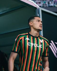 a man standing in front of a crowd wearing an orange and green striped soccer shirt