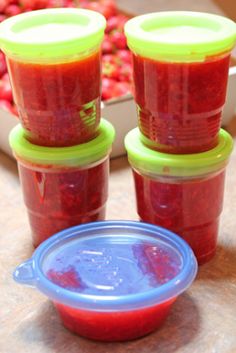 four plastic containers filled with red sauce sitting on top of a table next to some strawberries