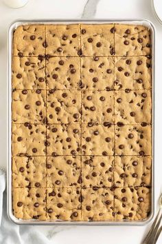 a pan filled with chocolate chip cookie bars on top of a white table next to silverware