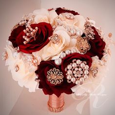 a bridal bouquet with red roses, pearls and brooches on display in a white room