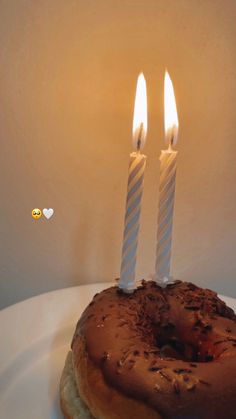 a donut with two lit candles on it sitting on top of a white plate