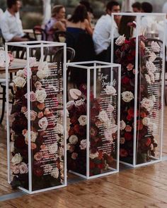 three clear boxes with flowers on them sitting on a wooden floor in front of people