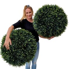 a woman holding two large round bushes in her hands, both with their arms around each other