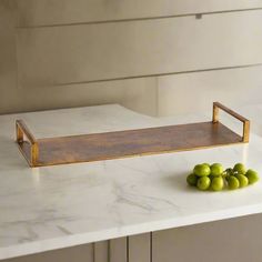 some green fruit on a white counter top with a wooden tray in the middle that is holding grapes