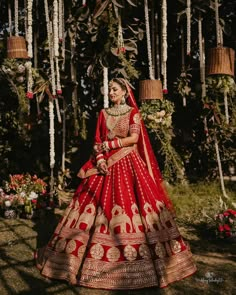 a woman in a red and gold bridal gown standing under some trees with flowers