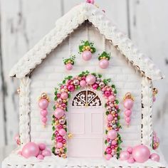 a white gingerbread house with pink and gold decorations on the front door is shown