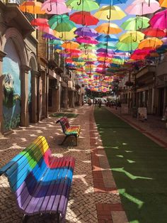 many colorful umbrellas are hanging from the ceiling in an alleyway with benches on both sides