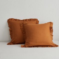 two brown pillows with ruffled edges on a white bed in front of a wall