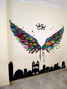 a wall painted with colorful wings and a crown on top of the cityscape