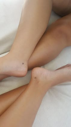 two women laying on top of a bed next to each other with their legs crossed