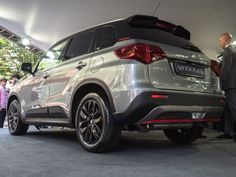 the rear end of a silver suv parked in a garage with people looking at it