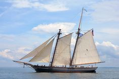 a large sailboat with white sails on the water in front of blue sky and clouds