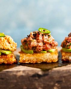 three small sandwiches with meat and vegetables on them sitting on top of a piece of wood