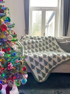 a christmas tree is next to a couch with a crocheted blanket on it