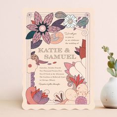 a wedding card with flowers on it next to a potted plant and white vase