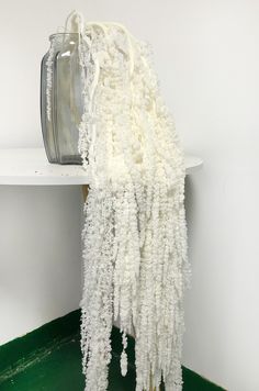 a vase sitting on top of a shelf next to a pile of white yarn hanging from it's side