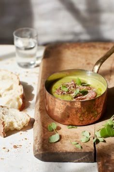 a copper bowl filled with soup on top of a wooden cutting board next to bread