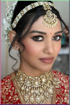 a woman in a red and gold bridal outfit with jewelry on her head, looking at the camera