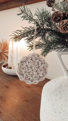 some pine cones are in a white vase on a wooden table next to other christmas decorations