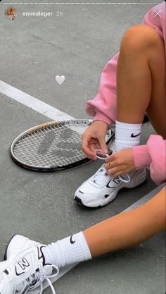 a tennis player tying her shoes on the court while sitting next to a racquet