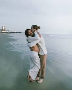 two women hugging on the beach in front of the ocean with buildings in the background