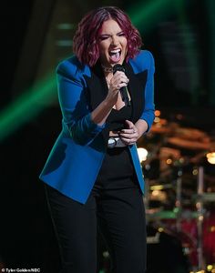 a woman singing into a microphone while standing in front of a stage with green lights