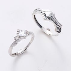 two silver rings sitting next to each other on top of a white surface with a diamond in the middle