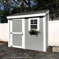 a white shed with a window and flower box on the door is next to a fence