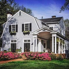 a white house with black shutters and flowers in the front yard