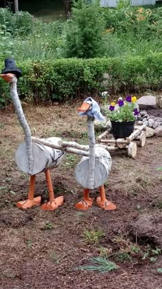 two birds are standing in the dirt near some plants and flowers, one is wearing a hat