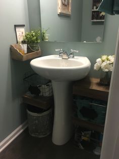 a white sink sitting under a bathroom mirror next to a wooden shelf filled with flowers