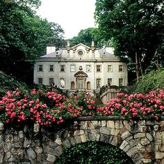 a large white house with pink flowers on the front and side of it near a stone bridge