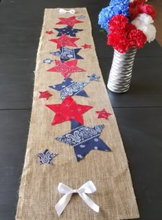 a table runner with red, white and blue stars on it next to a vase filled with flowers