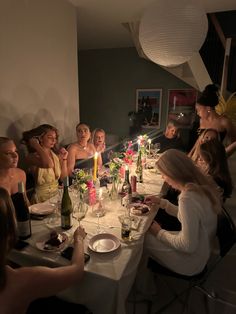 a group of women sitting around a dinner table with candles in their hands and plates on the table