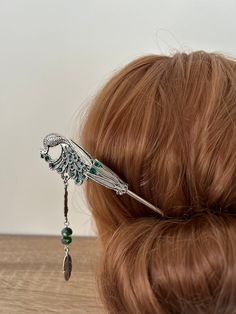 Channel your inner goddess with this enchanting peacock hair stick. 🌺🦚 Its emeral green hues, intricate feather details, and hanging feather tassel. A mesmerizing hair accessory that will turn heads. Peacock hair stick Peacock Feather Hair Stick, Emerald Green Hair Stick, Feather Hair Pin Peacock Hair Jewelry or can be used as a bookmark.  Antique Silver in color with Green Rhinestones and 8mm glass crystal beads. Approximate Length 17cm x 2.8cm. The peacock is one sided but the backing metal Peacock Bookmark, Emerald Green Hair, Emerald Hair, Peacock Hair, Peacock Jewelry, Feather Hair, Flower Hair Comb, Bun Hair, Bun Hairstyles For Long Hair