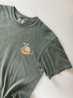 This is the kind of t-shirt your friends (and hikers & coffeeshop goers & fellow people perusing the library) will ask you about.  "Is that a National Parks t-shirt?" "What is the moose holding?" "Is that a mouse?" (Please tell them it's a rat, named Rat.) This is a t-shirt with a story. The story of two friends, one canoe, and somewhere to go. (Where are they going? We'll have to find out.) This t-shirt starts the saga. The saga of Moose in the Canoe (feat. Moose's friend, Rat. Rat is not a mouse.)  Printed on the Comfort Colors 1717 crew neck tee, which has nice outdoorsy colors for those of us who dream about hiking Glacier National Park but end up staring out the window drinking coffee. The t-shirt was made using ethically grown and harvested 100% US cotton. Pre-shrunk (so you never ha A Rat, Mouse Print, Two Friends, Drinking Coffee, The Library, Looks Vintage, Crew Neck Tee, Dye T Shirt, Tshirt Colors