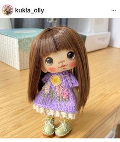 a doll with long brown hair wearing a purple knitted dress and green booties