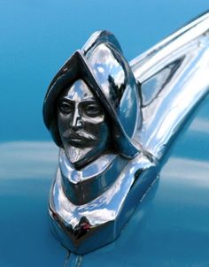 the hood ornament is on top of a shiny blue car, and it looks like a woman's head