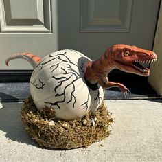 a fake t - rex sitting on top of an egg in front of a door