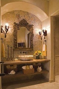 a bathroom with stone walls and an arched doorway leading to the sink area is lit by two sconces