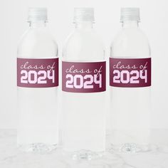 three clear water bottles with class of 202 printed on them, sitting on a marble surface