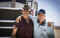 two men standing next to each other in front of a semi - truck, smiling