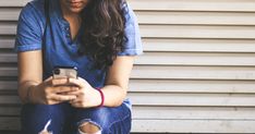 a young woman sitting on the ground looking at her cell phone while wearing ripped jeans