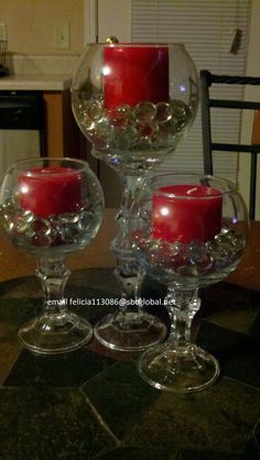 three wine goblets filled with red candles on top of a black marble table