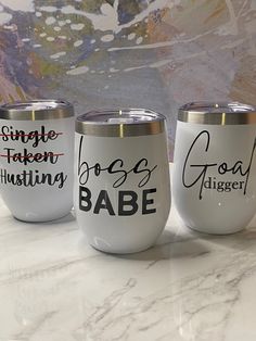 three wine glasses with different sayings on them sitting on a marble countertop in front of a painting