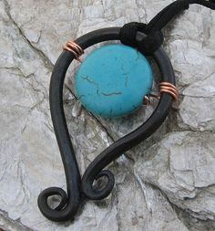 a piece of jewelry sitting on top of a rock next to a metal hook with a blue stone in it