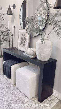 a black and white console table with two stools next to it in front of a mirror